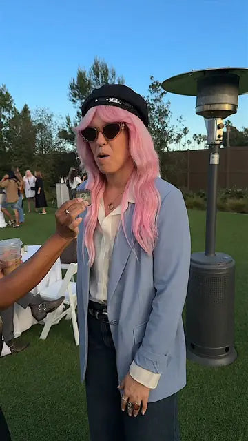 An attendee with long pink hair, a black cap and sunglasses mid-conversation on the lawn